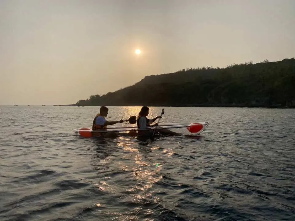 兩人乘坐透明獨木舟，在小琉球夕陽餘暉中划行，享受金色海面與浪漫日落的絕美景色。