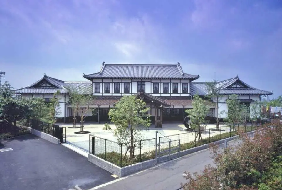 Một tòa nhà kiểu Nhật truyền thống trong khuôn viên Bảo tàng Đường sắt Kyoto, được bao quanh bởi cây xanh tươi tốt dưới bầu trời xanh trong, mang đến trải nghiệm văn hóa phong phú.