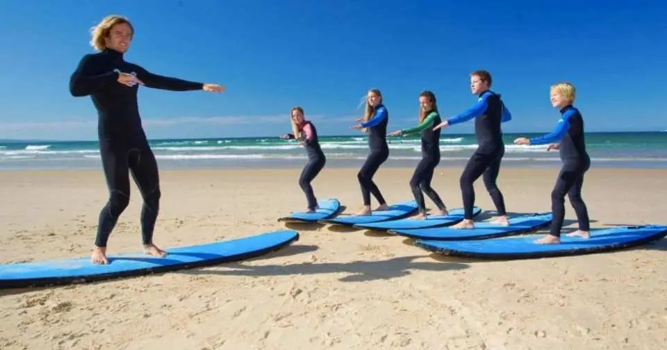 On Torquay beach in Melbourne, a professional surfing instructor demonstrates surfing stances to a group of students, imparting basic knowledge and safety essentials for the 2-hour surfing lesson.
