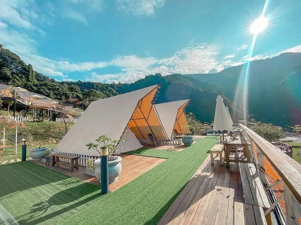台中覓靜莊園高山免裝備露營區，兩座白色現代豪華帳篷與木製平台戶外休憩區，坐擁壯麗山景，陽光普照。