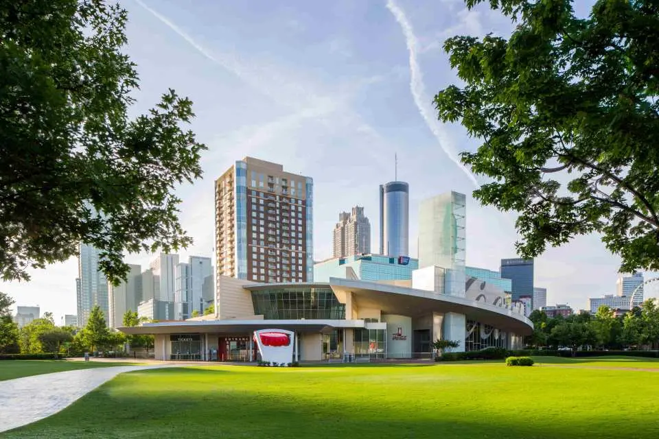 มุมมองตอนกลางวันของอาคารพิพิธภัณฑ์ World of Coca-Cola ที่ทันสมัยในแอตแลนตา ล้อมรอบด้วยสนามหญ้าสีเขียวชอุ่มและฉากหลังเป็นตึกระฟ้าของเมือง พร้อมกระป๋องแดงยักษ์
