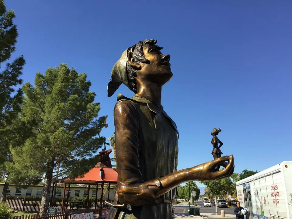 Unique outdoor art sculpture of a distinctive figure against green trees and blue sky in Boulder City's historic district, enriching your self-guided tour's visual journey.