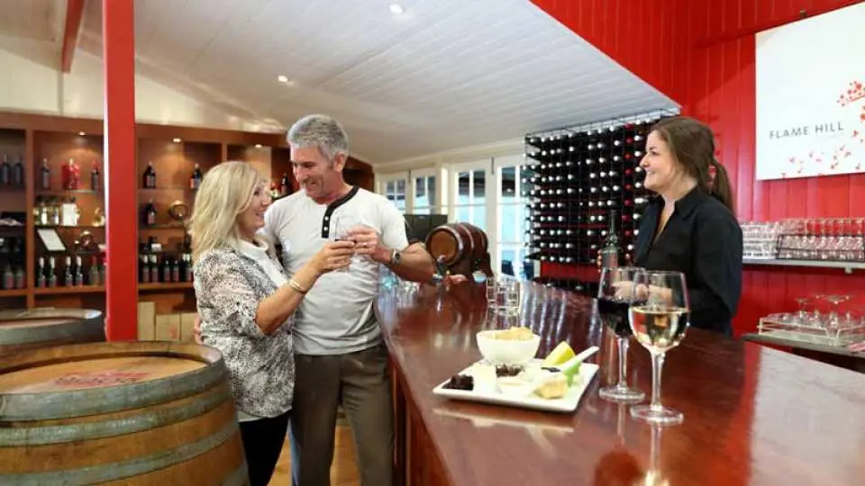 An elderly couple enjoying glasses of wine at Flame Hill Winery, with a plate of assorted cheese and glasses of wine on the table and a sommelier standing at the table