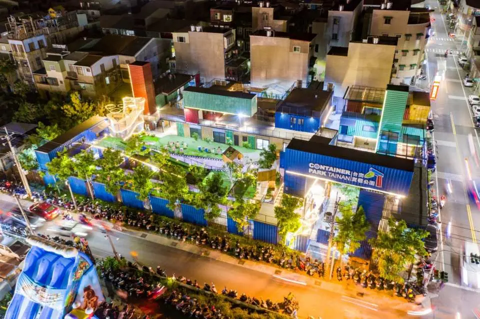 Aerial night view of Tainan Container Park, brightly illuminated container buildings and green spaces shining amidst the city lights, perfect for family fun.