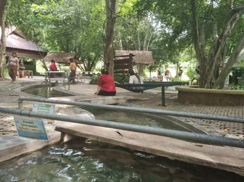 Tourists comfortably enjoying a foot bath by traditional Thai-style shelters at San Kamphaeng Hot Spring, a relaxing mineral bath experience.