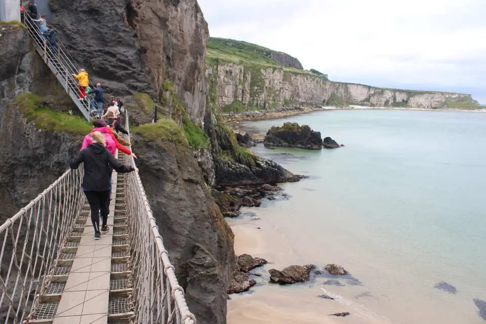 นักท่องเที่ยวเดินข้ามสะพานเชือกคาร์ริก-อะ-รีด ในไอร์แลนด์เหนือ ซึ่งเป็นทางเดินที่น่าตื่นเต้นแขวนอยู่ระหว่างหน้าผา มองเห็นวิวอ่าวสีฟ้าครามเบื้องล่าง