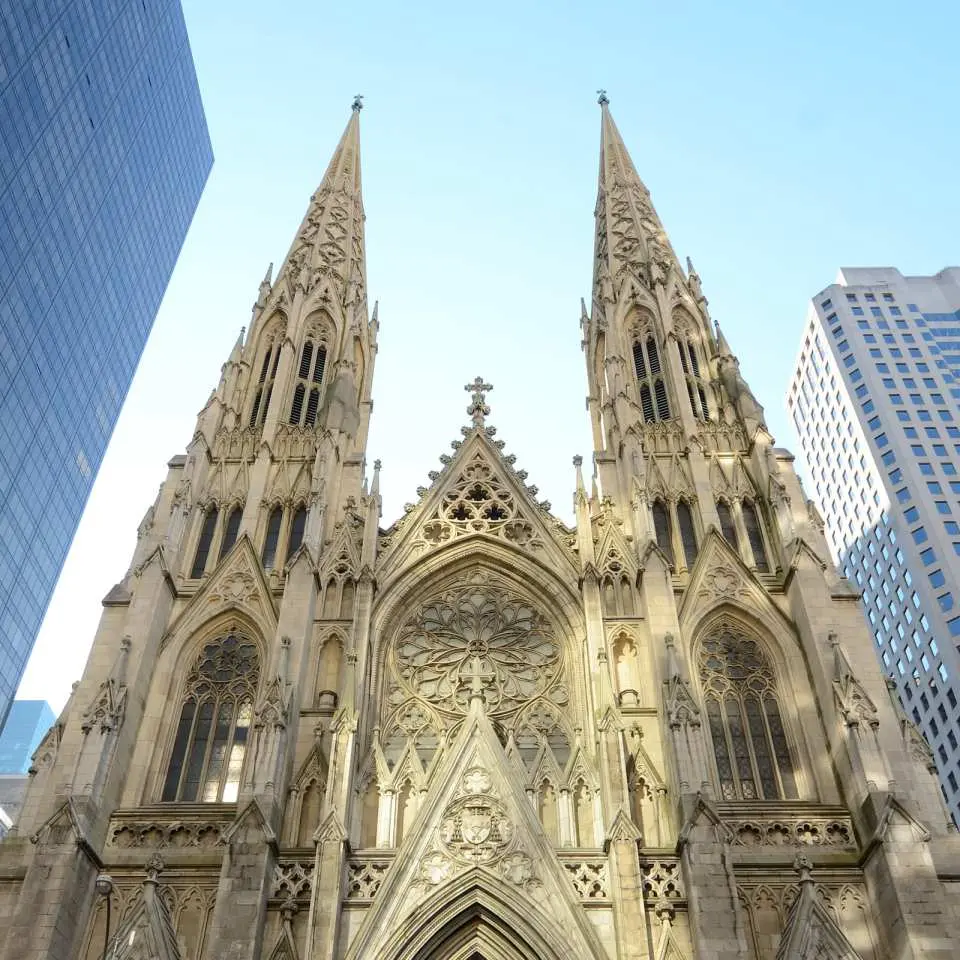 The magnificent Gothic exterior of St. Patrick's Cathedral in New York, with its two towering spires reaching into the blue sky, showcasing its grandeur as a city landmark, perfect for an audio-guided exploration.