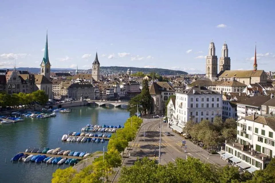 Panoramic view of Zurich cityscape along the Limmat River during a half-day old town tour, featuring Fraumünster, Grossmünster twin towers, and historic buildings, showcasing Switzerland's beautiful waterfront.
