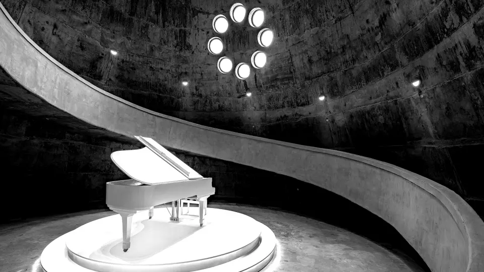 An art space inside Vietnam's World of Coffee Museum, featuring a white grand piano on a central circular stage, with a spiral ramp and round skylight, exuding modern artistic flair.