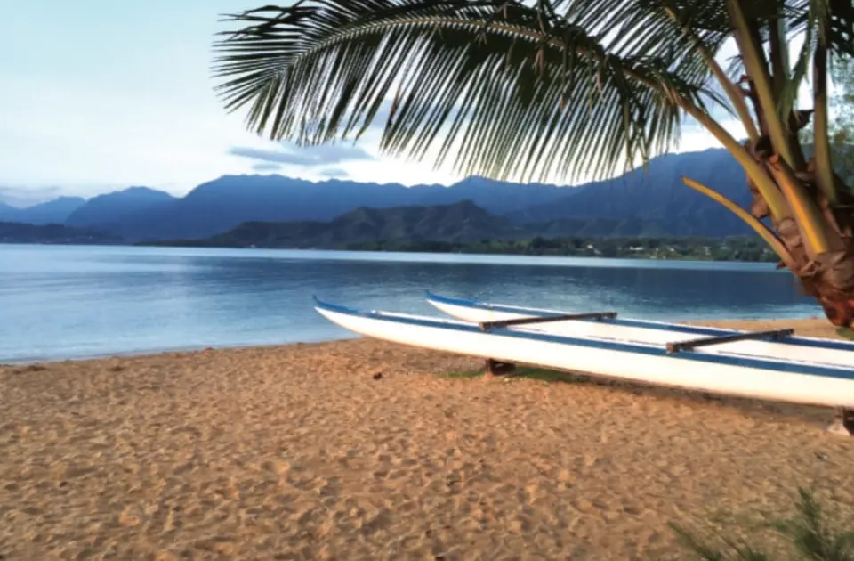 Two canoes resting on the soft sandy beach of Kualoa Secret Island, Oahu, Hawaii, with distant mountains, showcasing the serene and natural tropical scenery.