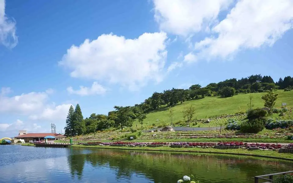 日本六甲GREENIA運動公園廣闊的湖泊景觀，青山綠樹環繞，藍天白雲倒映湖面，展現自然休閒之美。