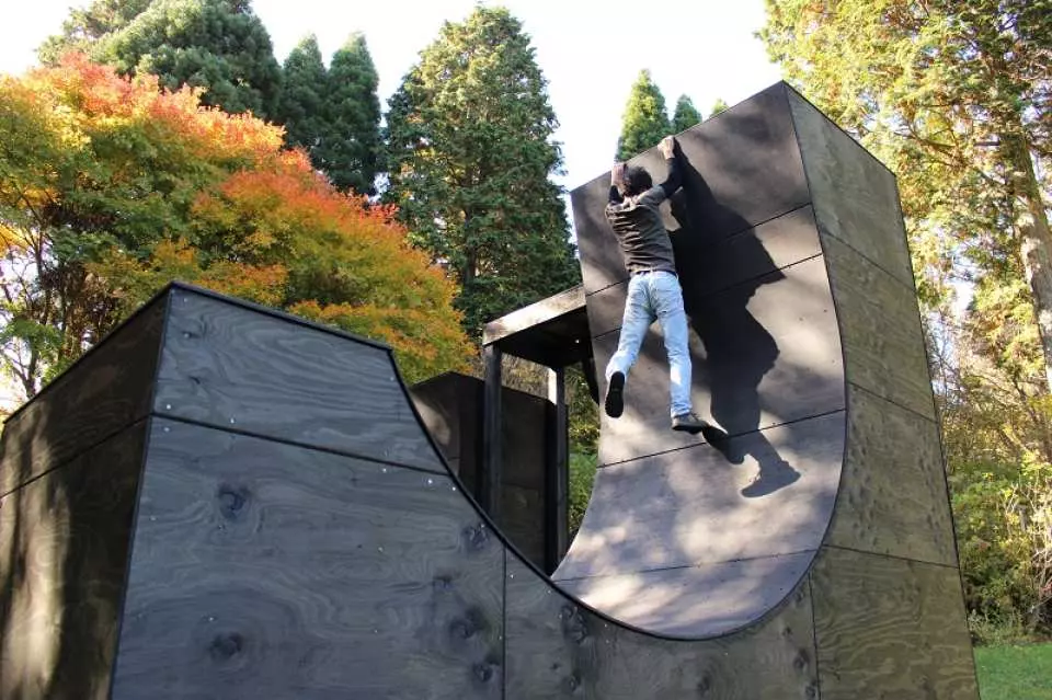 一名遊客在日本六甲GREENIA運動公園挑戰高難度的黑色弧形攀爬牆，展現體能與力量，背景為秋季林木。