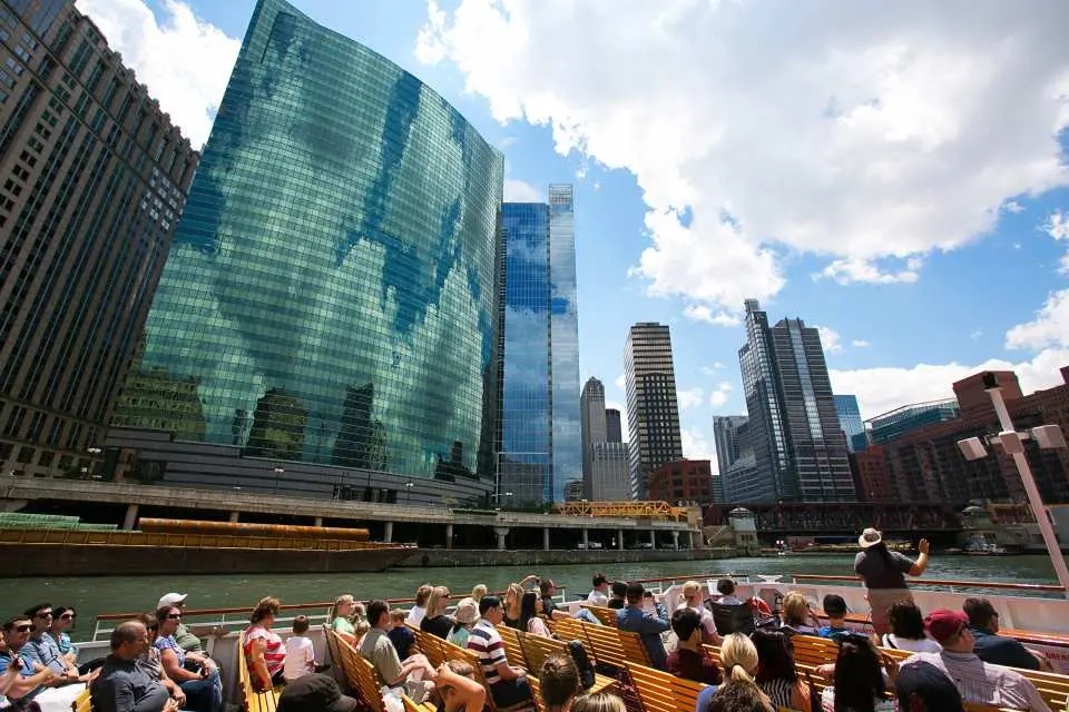 Tourists on a Chicago River architectural cruise admire towering skyscrapers along both banks, experiencing the city's unique architectural beauty and waterfront scenery.