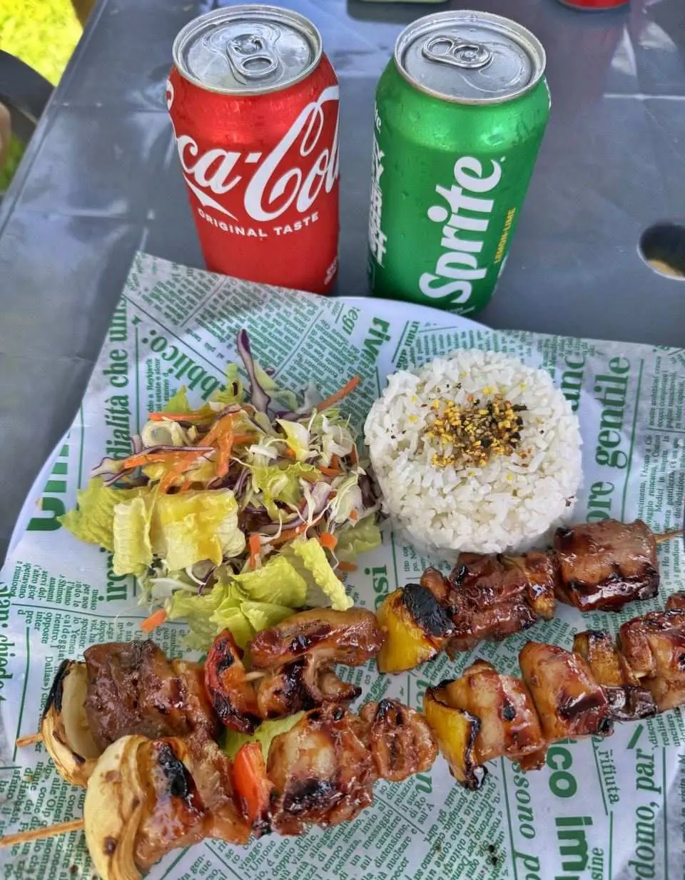 A delicious Saipan meal set featuring grilled meat and vegetable skewers, fluffy rice, fresh salad, and refreshing soft drinks, perfect for refueling after Grotto adventures.