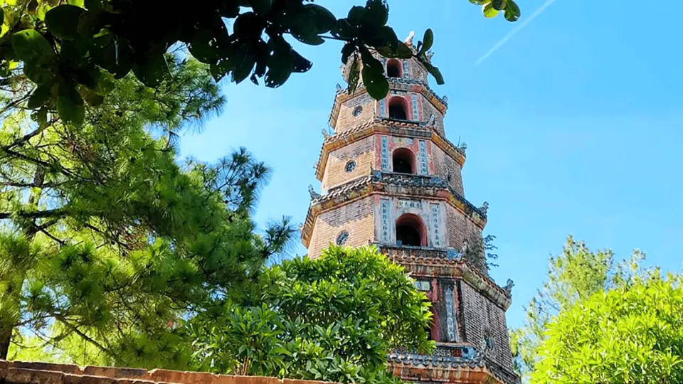 The majestic seven-story Thien Mu Pagoda tower in Hue's ancient capital, featuring unique traditional architecture and intricate brick carvings against a clear blue sky, surrounded by lush trees, showcasing its solemn beauty.