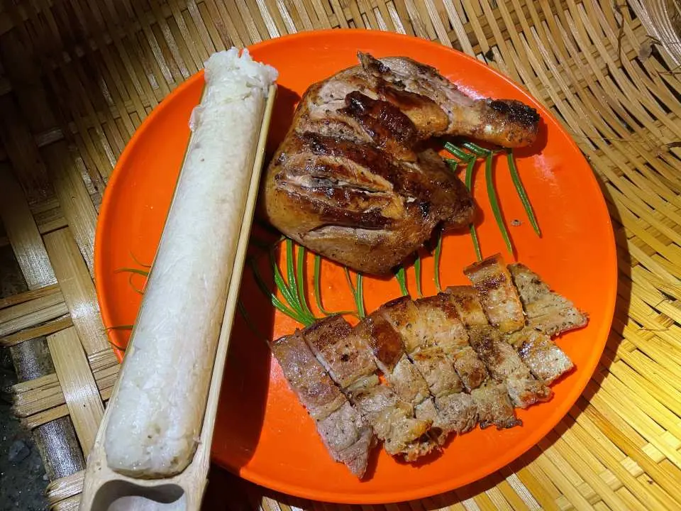 A vibrant orange plate presenting a delicious Hualien BBQ dinner after night prawning, featuring grilled chicken, sliced meat, and traditional bamboo-tube rice on a woven mat.