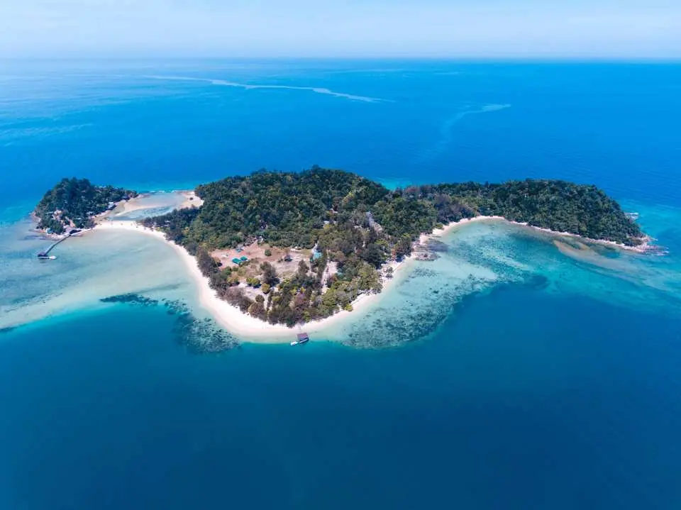 Aerial view of the seahorse-shaped Dinawan Island in Sabah, Malaysia, showcasing its lush forests, pristine white sand beaches, and crystal-clear turquoise waters perfect for snorkeling.