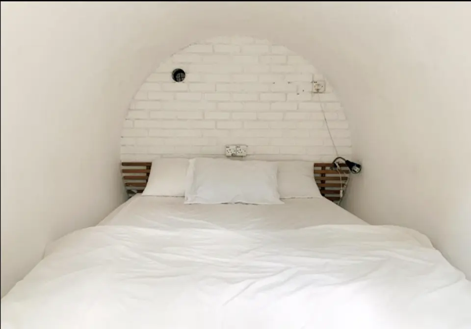 Clean and minimalist interior of a Time Capsule Retreat capsule room in Sungai Lembing, featuring a comfortable white bed with an arched brick headboard for a cozy stay.