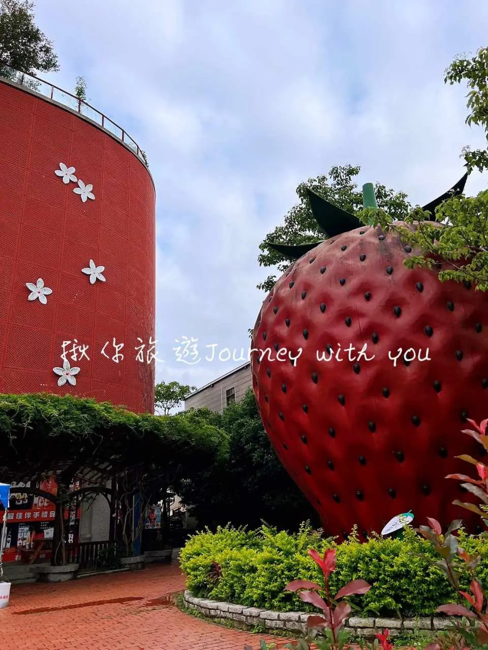 A whimsical giant strawberry sculpture complementing a vibrant red building at a Miaoli strawberry-themed attraction, inviting visitors to enjoy strawberry picking and scenic tours in this charming region.