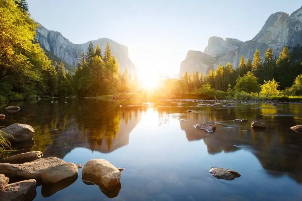 Serene Merced River in Yosemite National Park, reflecting mountains and forests under golden sunset or sunrise hues, a tranquil highlight of your 2-day trip from Los Angeles.