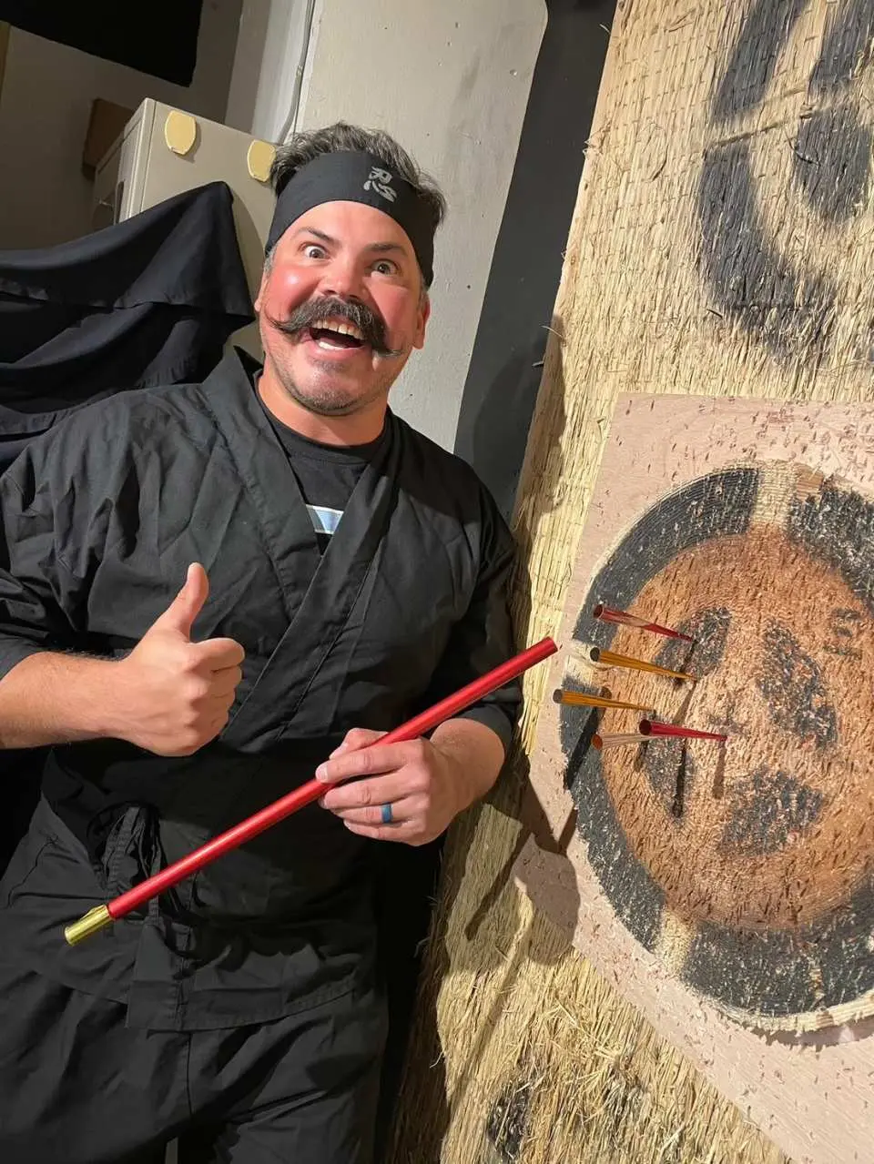 一位開心滿足的遊客在東京淺草忍者體驗咖啡館穿上忍者服裝，成功使用吹箭筒射中靶子，並豎起大拇指。