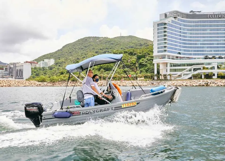學員與導師駕駛二級遊樂船喺香港仔海面乘風破浪，遠處可見壯麗嘅海岸線、山巒與城市建築群，風景宜人。