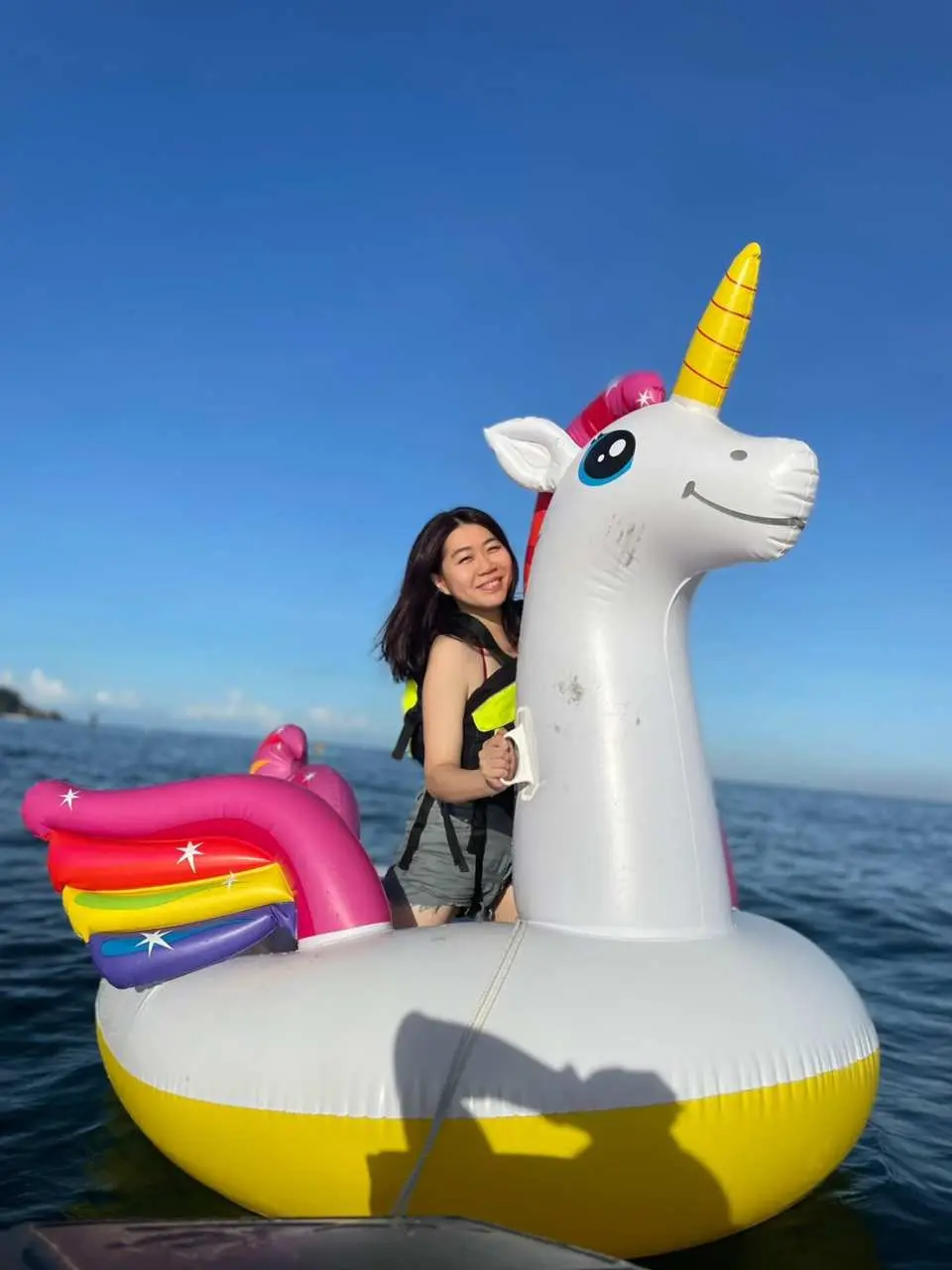 一位女士在小琉球清澈海面上，開心地乘坐彩虹獨角獸大型浮具，體驗夢幻又有趣的拍照時刻。