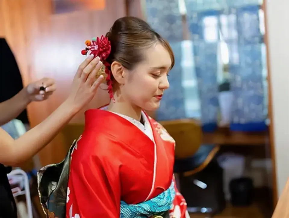 沖縄那覇の和服レンタル体験で、プロのスタイリストが女性客に繊細なヘアスタイルと髪飾りを施し、完璧な浴衣姿を完成させます。