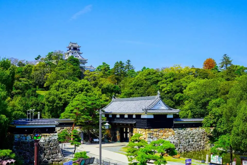 青空の下、豊かな緑に囲まれた日本の高知城全景。壮大な城門と天守閣が堂々とした姿を見せています。