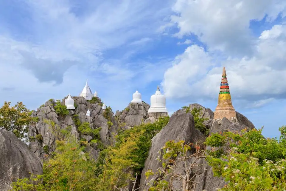 Wat Phrabat Pu Pha Daeng in Lampang, Northern Thailand, featuring multiple white pagodas and a colorful stupa perched on rugged mountain peaks under a bright blue sky, a stunning highlight of the Lampang day trip.