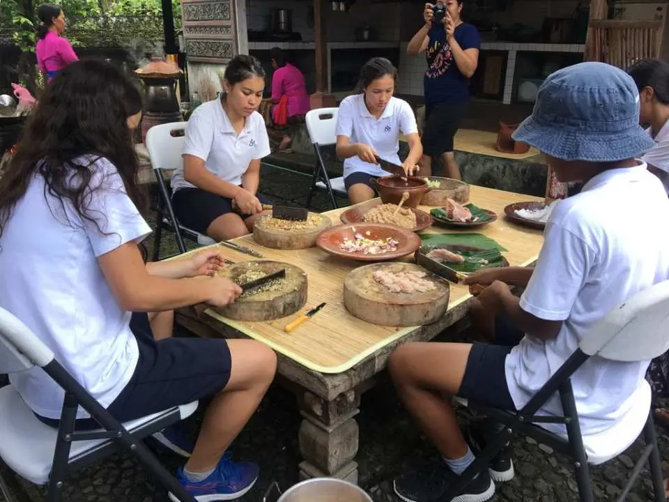 Young participants in a Balinese village cooking demonstration attentively prepare ingredients, delving into the secrets of Balinese cuisine and experiencing Ubud's culture.