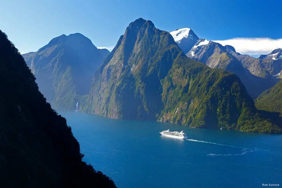 搭乘遊覽車前往遊覽 Milford Sound 米佛峽灣。專車前往紐西蘭最大、世界排名第五的 Fiord land National Park「峽灣國家公園」，毛利語稱米佛峽灣為 PIOPIOTAHI，佔地面積達 125 萬公頃於 1986 年已被授予世界遺產區。此外，前往密佛頌峽灣的道路被人稱為全世界風景最好的高地公路之 一。沿途行車欣賞峽灣國家公園內的壯麗景緻，通往峽灣的道路兩旁覆蓋著紐西蘭原始冷溫帶雨 林，其中主要樹種是銀山毛櫸，葉子如指甲般大小，樹幹長有銀白色的樹皮，專車行經峽灣國家公 園內最大的天然草原-埃格林頓山谷 Eglinton valley、鏡湖 Mirror Lake、諾布斯平原 Knobs Flat、 全長 1.27 公里的荷馬隧道 Homer Tunnel 等，午間抵達 Milford Sound 米佛峽灣，