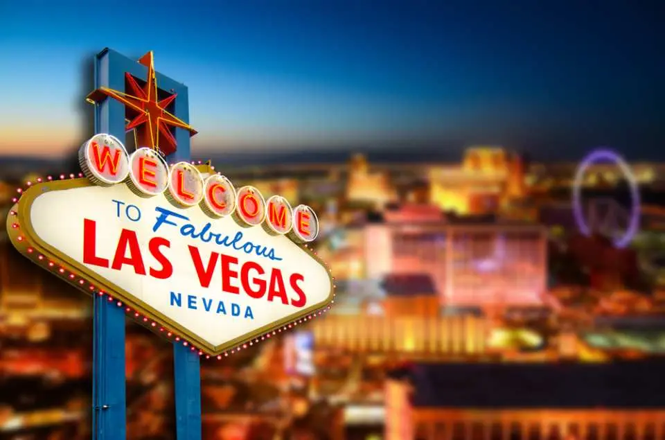 夕暮れ時に輝く有名な「Welcome to Fabulous Las Vegas Nevada」の標識。背景にはぼやけた賑やかな街の明かりがあり、忘れられないアメリカ西部冒険ツアーの出発点を示しています。