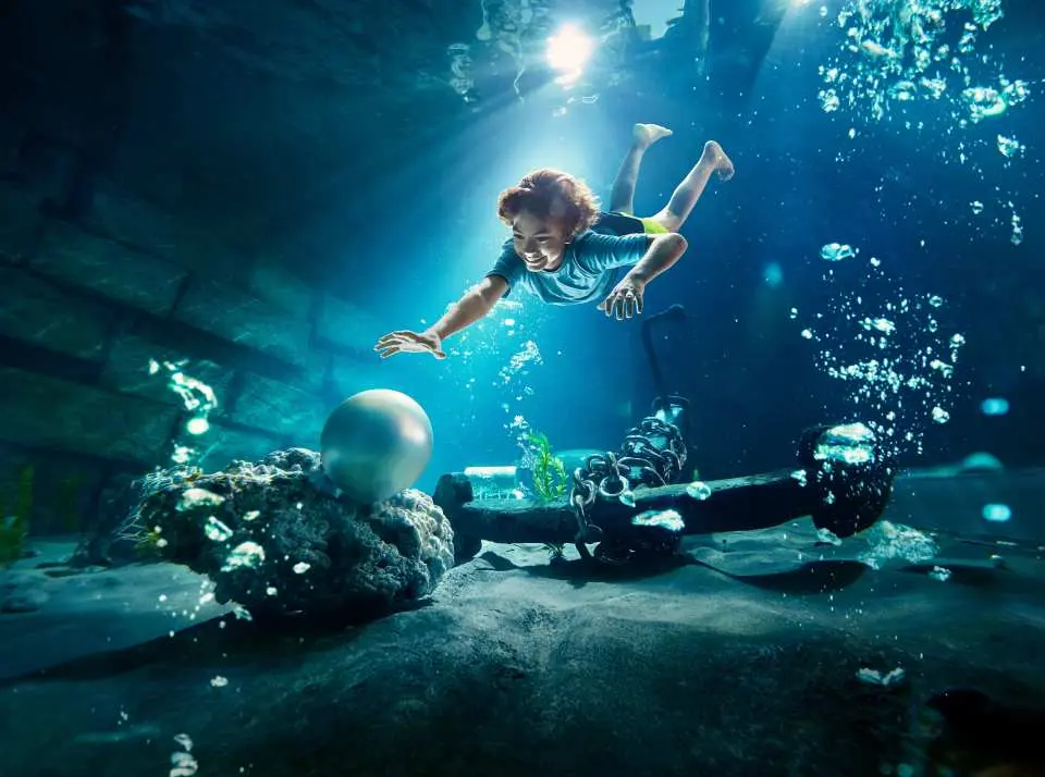 Trải nghiệm dưới nước đầy sống động tại Yas Waterworld Abu Dhabi, cho thấy một đứa trẻ đang vươn tay lấy một viên ngọc trai lớn, tượng trưng cho điểm tham quan lặn ngọc trai độc đáo.