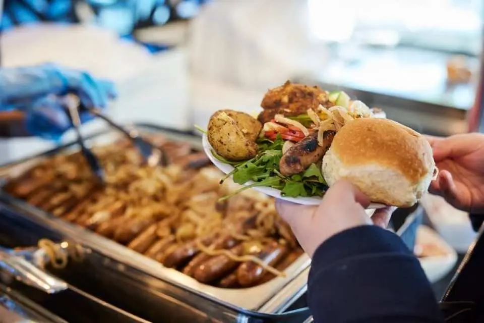 A plate with a traditional Australian BBQ lunch, including sausages, roasted potatoes, fresh salad, and a bread roll, served from the buffet on the Sydney Harbour Discovery Lunch Cruise.