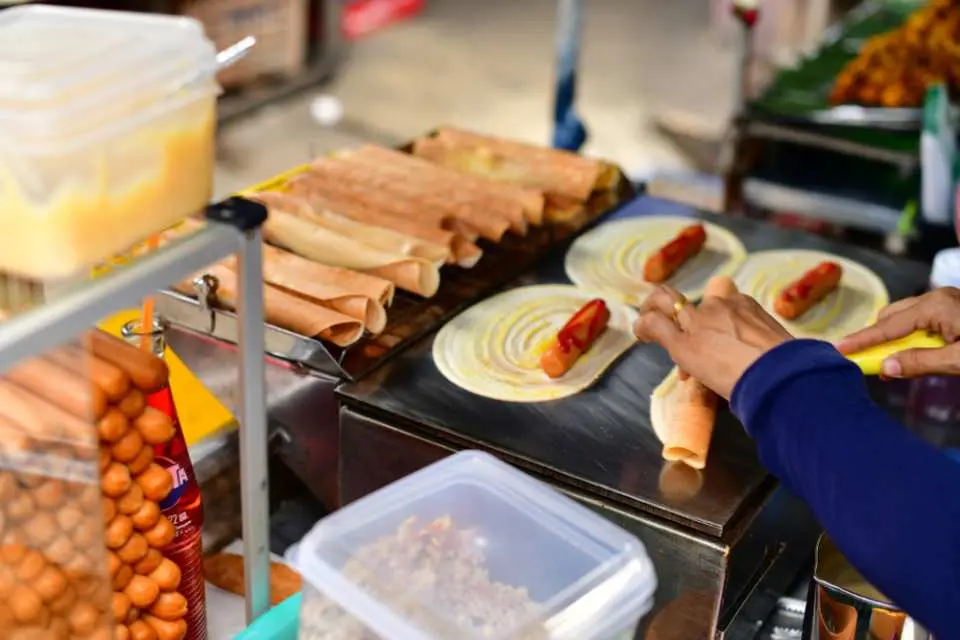 Một người bán hàng tại Chợ cuối tuần Chatuchak đang khéo léo làm bánh crepe Thái với nhiều loại nhân trên chảo nóng, một món ăn vặt đường phố nổi tiếng được chế biến tươi tại Bangkok.