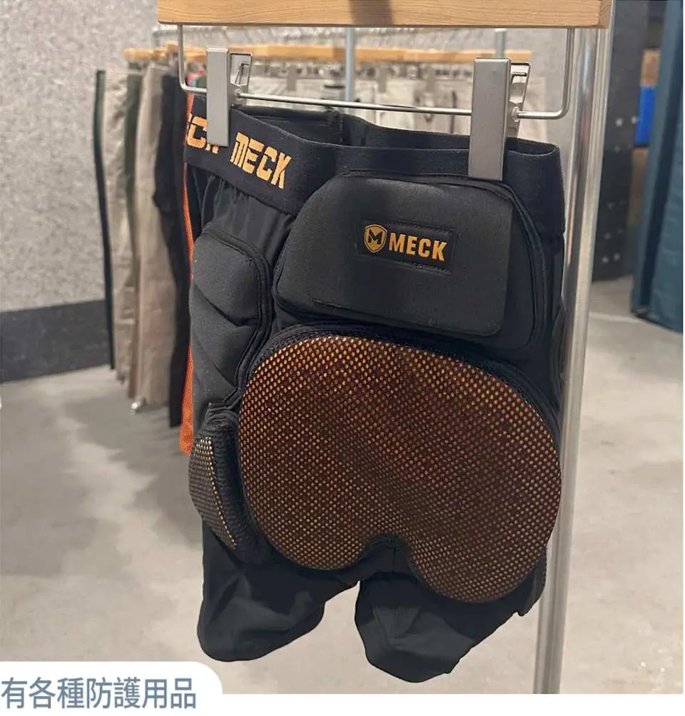 展示架上掛著黑色的滑雪防護褲，有厚實的護墊，下方文字說明「有各種防護用品」，確保遊客滑雪安全。
