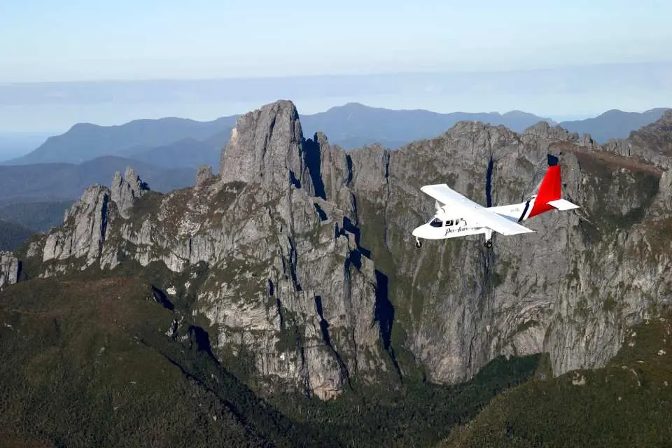 A small scenic plane flies over Tasmania's rugged southwestern mountains, offering breathtaking aerial views of the pristine wilderness on this land and sea day tour.