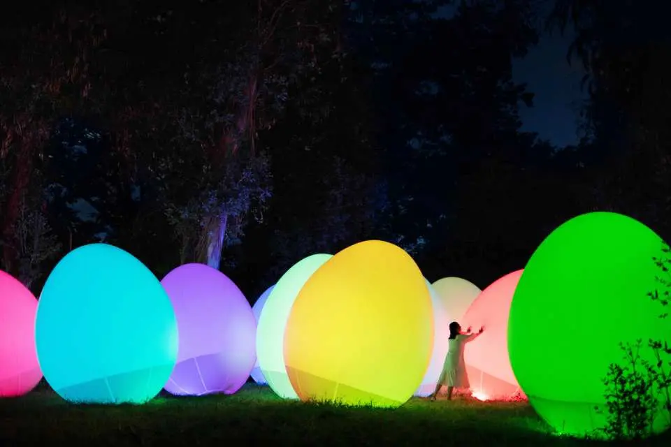 Visitors immerse themselves in an interactive display of giant, brightly colored glowing ovoid art installations at teamLab Botanical Garden Osaka's night exhibition.