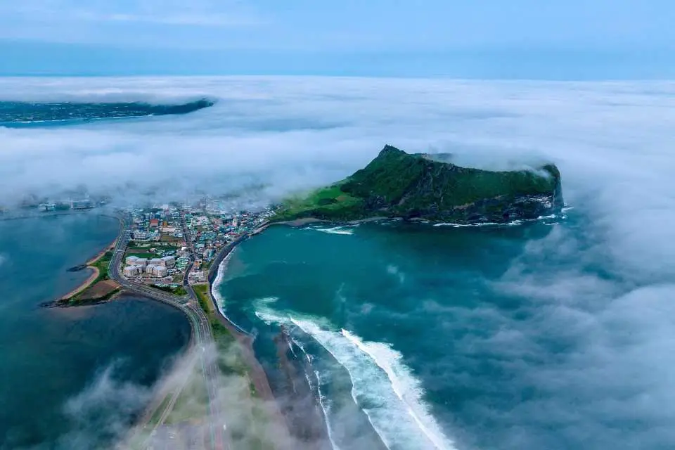 【在世界的盡頭，遇見大地最初的模樣：城山日出峰】如果說牛島是遺落在海上的珍珠，那麼城山日出峰，就是守護這片蔚藍大海的「綠色王冠」。  這座由海底火山噴發而成的巨岩，如同一座大自然的祭壇，孤傲而壯麗地屹立在濟州島的最東端。清晨時分，當第一道曙光劃破海平面的薄霧，金色的光芒灑落在火山口邊緣的 99 座尖峰上，那一刻，你會發現時間彷彿靜止了，只剩下浪潮拍打礁石的律動，以及內心深處那份久違的平靜。  沿著整齊的木棧道拾級而上，身側是翠綠的草甸，回頭一望，則是蜿蜒的海岸線與錯落有致的彩色屋頂。登頂後，眼前豁然開朗的巨大碗狀火山口，像是在訴說著數千年前大地的脈動。  在這裡，不一定要追趕日出的腳步。午後的微風、遠方牛島的身影，或是山腳下海女們充滿生命力的歌聲，都是城山日出峰給予旅人最溫柔的擁抱。來這裡走走吧，讓這份源自海洋與火焰的壯闊，重新填滿你對旅行的想像。