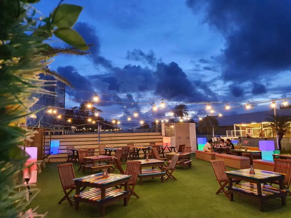 A charming outdoor dining and lounge area at The Tides Hotel Boracay during dusk, illuminated by warm string lights and offering comfortable wooden seating.