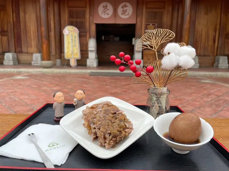 Local specialty braised dishes and tea eggs served on a black tray against a traditional wooden background, inviting visitors to savor a rich and authentic culinary experience at Fengyi Academy.