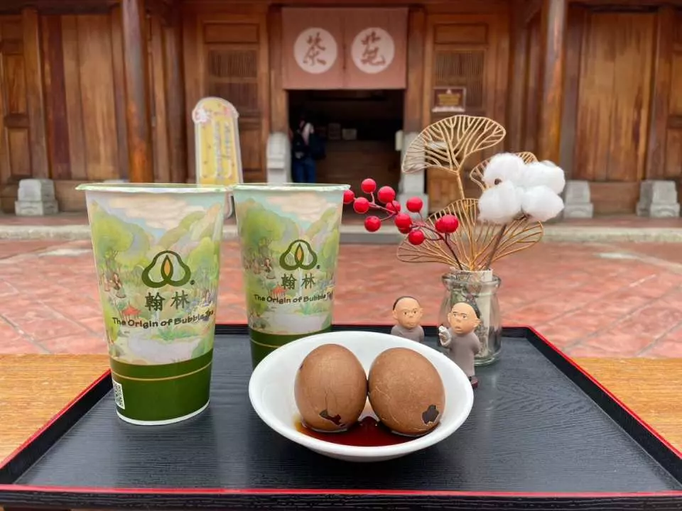 Specialty 'Fenglin' beverages and savory braised tea eggs served on a tray with adorable monk figurines, offering visitors a taste of local Taiwanese flavors at Fengyi Academy.
