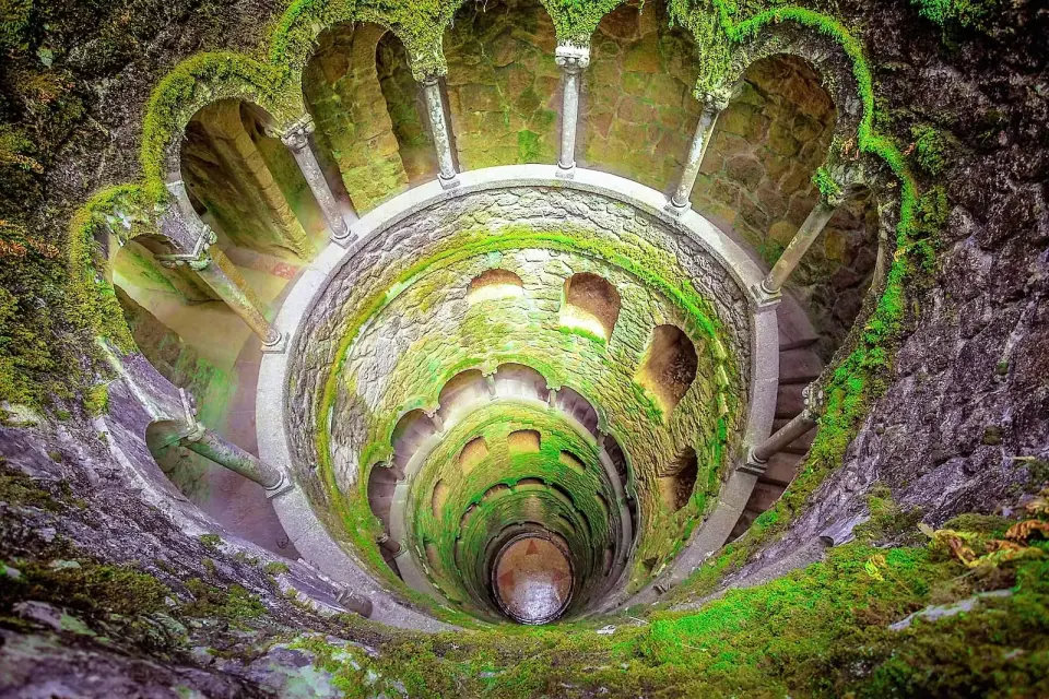Overlooking the mysterious Initiation Well at Quinta da Regaleira in Sintra, Portugal, its spiral staircase and moss-covered walls offer a profound historical experience on a guided tour.