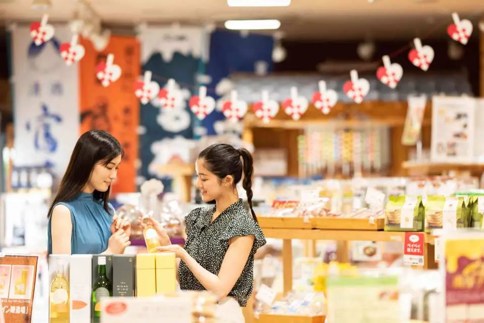 静岡の富嶽温泉花の湯にある土産物店で、二人の女性が地元の特産品や記念品を吟味し、ショッピングを楽しんでいます。
