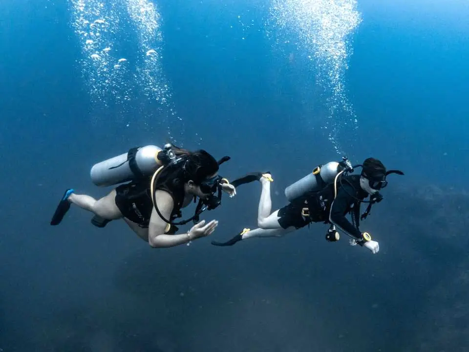 Two divers in Koh Tao, Thailand's open water diving course, guided by an experienced SSI instructor, learn and practice underwater communication skills.