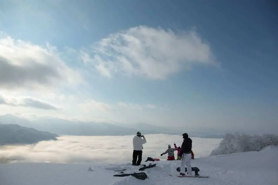 Skiers at the summit of X-JAM Takai Fuji Ski Resort in Nagano, admiring a spectacular sea of clouds, enjoying a unique experience blending skiing with nature.