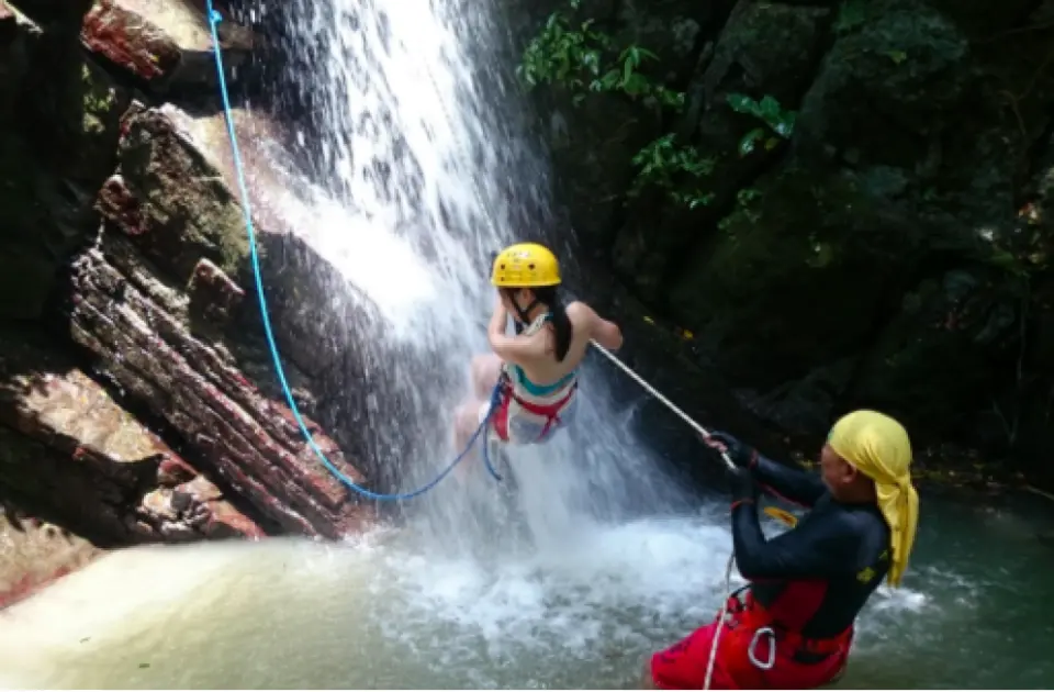 參加者在墾丁七孔瀑布專業教練指導下，戴著黃色頭盔與安全裝備，挑戰從瀑布中垂降而下，體驗清涼與刺激。