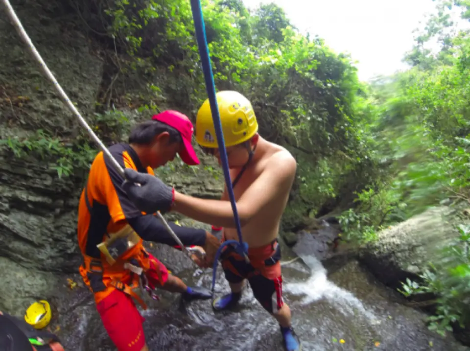 專業教練在墾丁七孔瀑布溯溪垂降體驗中，細心為學員檢查並調整安全裝備，確保活動安全與專業指導。