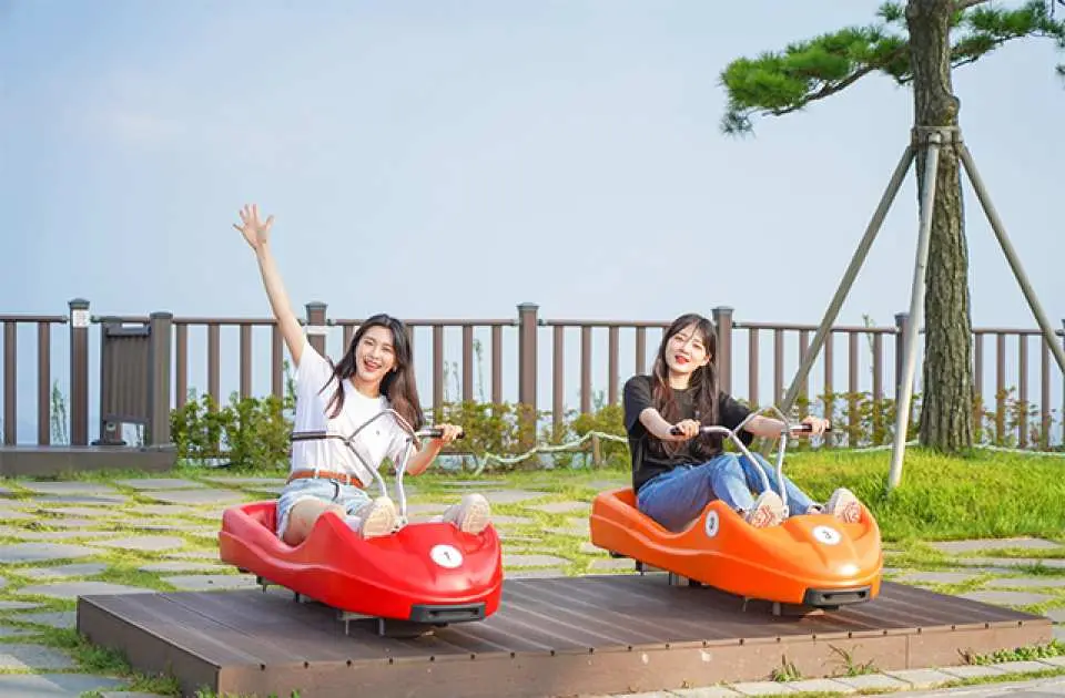 兩位遊客在江華島 LUGE 斜坡滑車出發區，戴著安全帽開心擺拍，準備體驗仁川首爾近郊熱門景點的滑車與纜車樂趣。